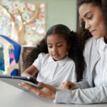 Black schoolgirl in an infant school learning with a female teacher using a tablet computer