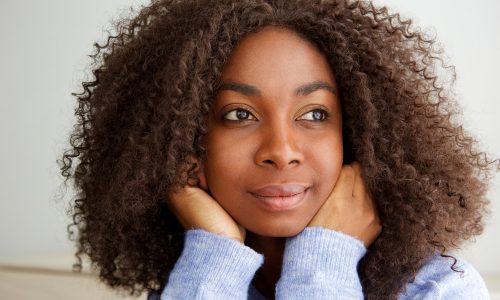 Close up attractive young african woman with curly hair looking away and thinking