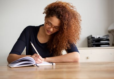 university student writing in book at home